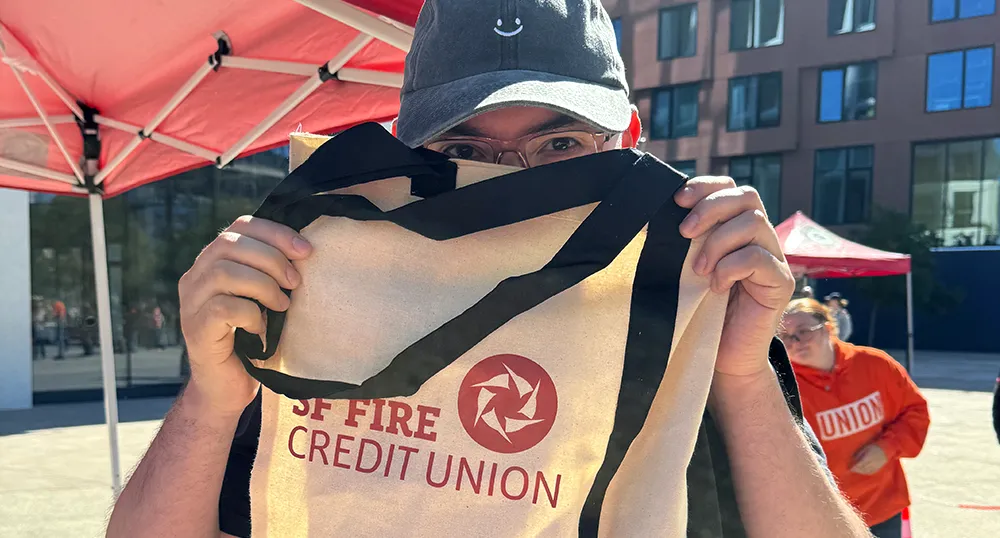 Man holding up a SF Fire tote bag at a community event