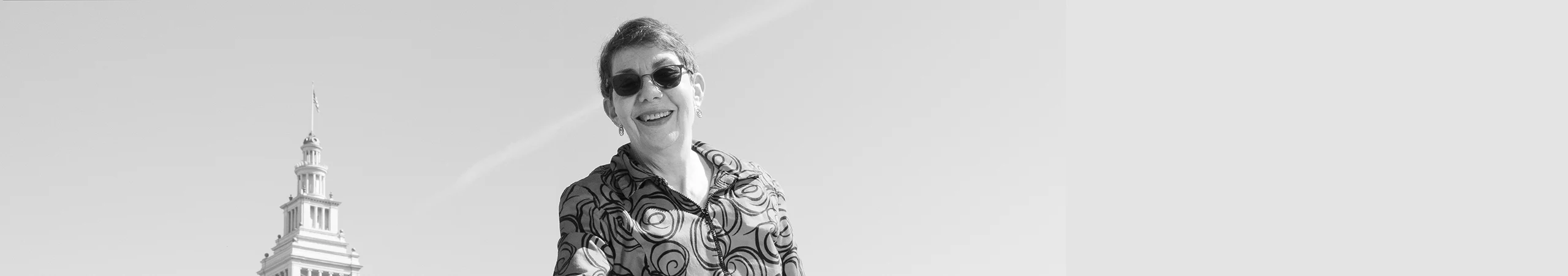 Woman stands confidently with a clear sky above. Spire of Embarcadero clock tower visible in the background.