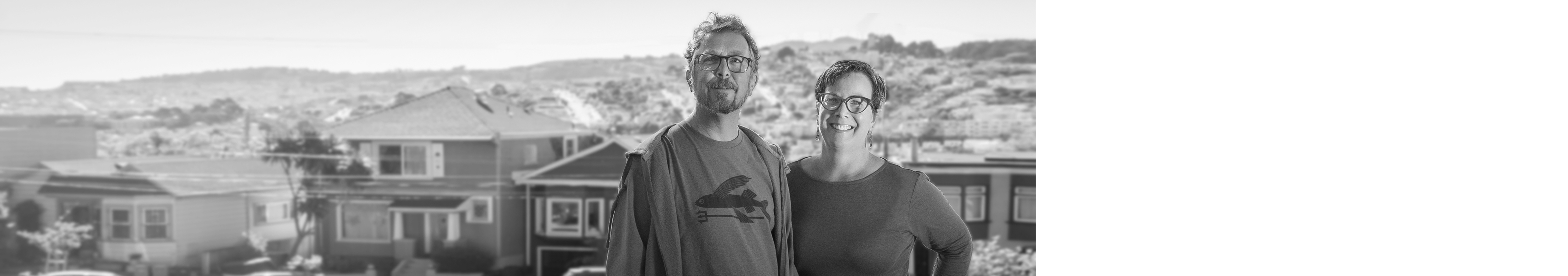 Couple stands in front of skyline and houses.