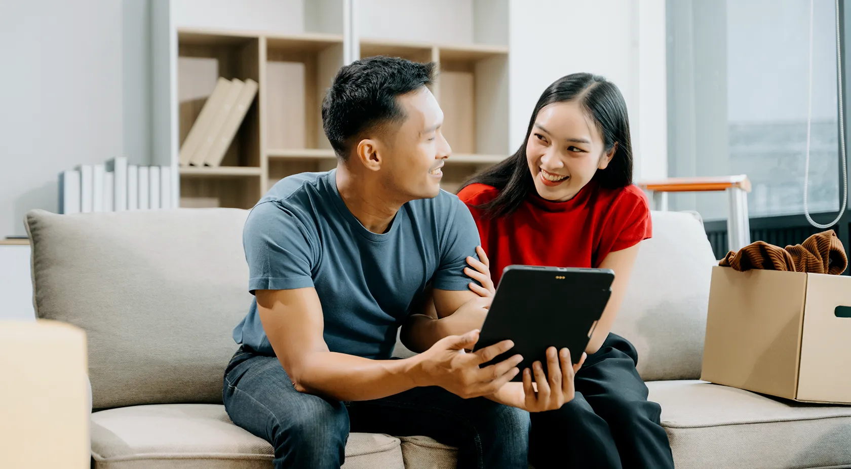 Asian couple on couch looking at tablet in their home