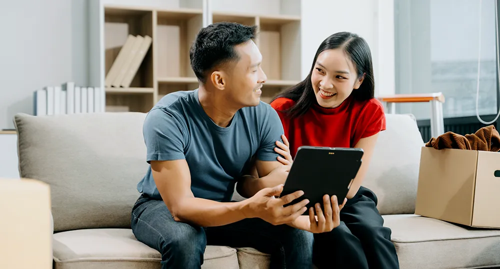 Asian couple on couch looking at tablet in their home