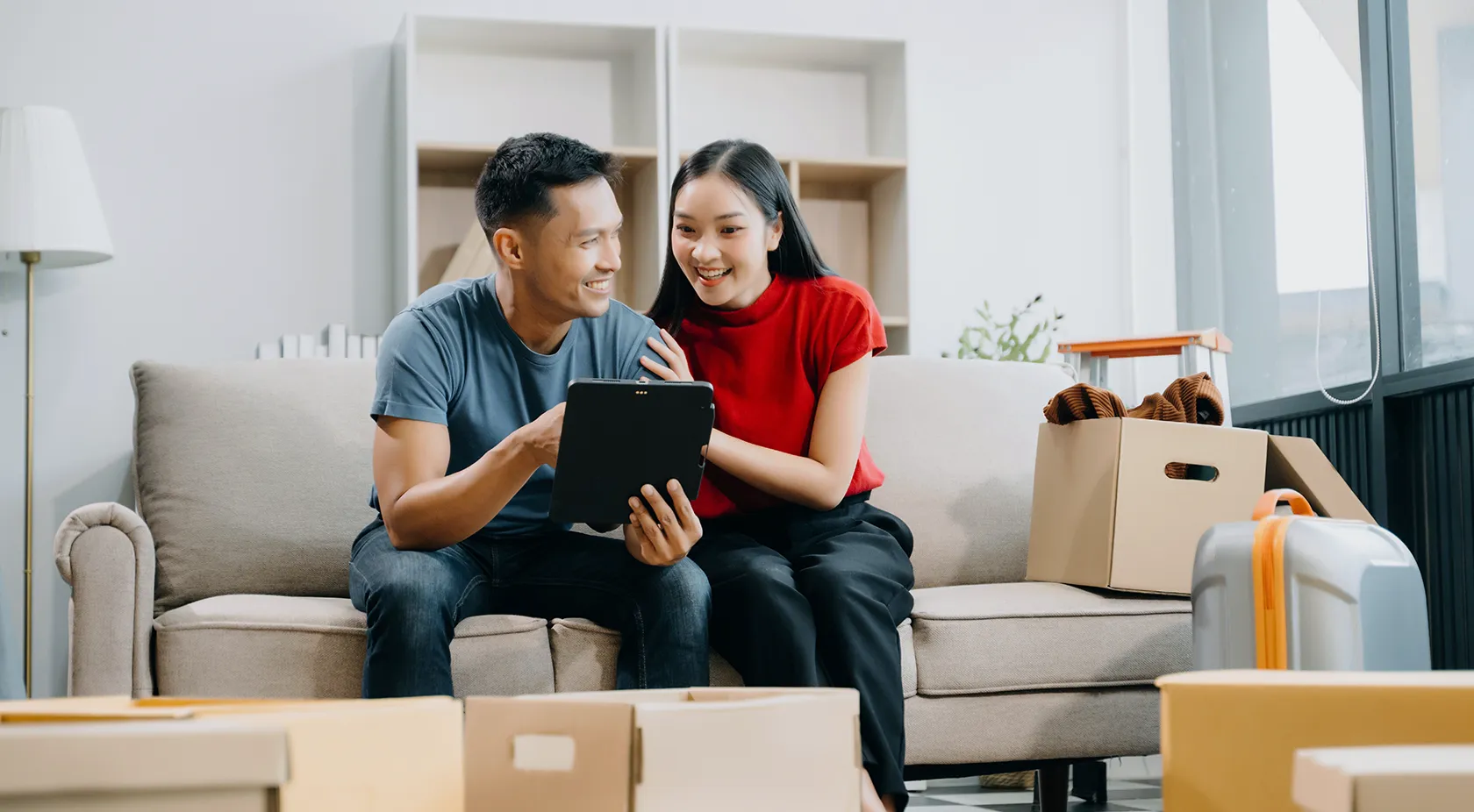 Asian couple on couch looking at tablet in their home with boxes surrounding them