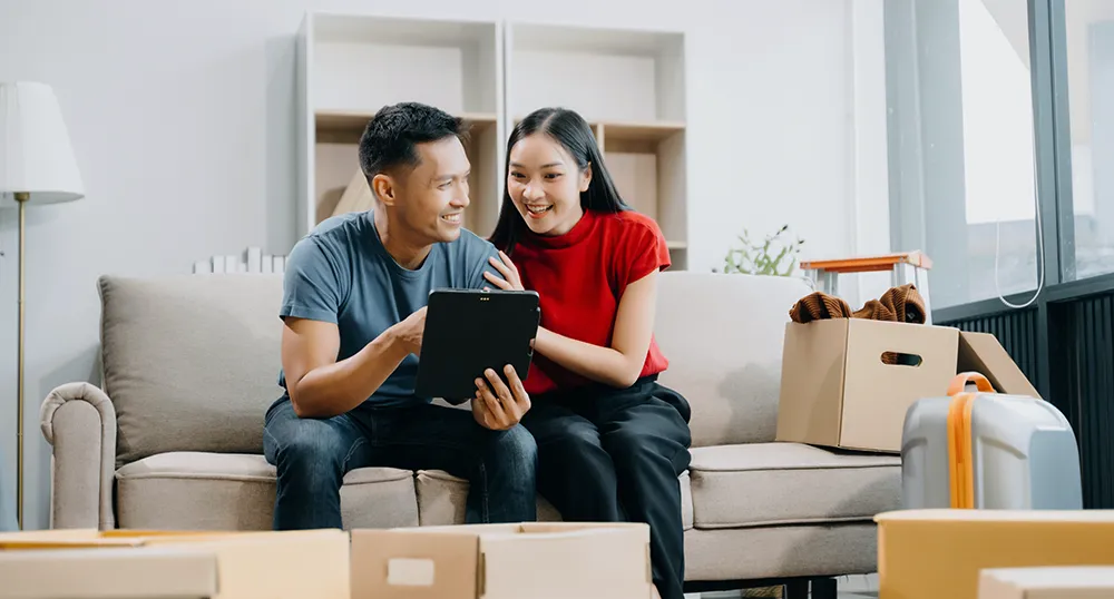 Asian couple on couch looking at tablet in their home with boxes surrounding them
