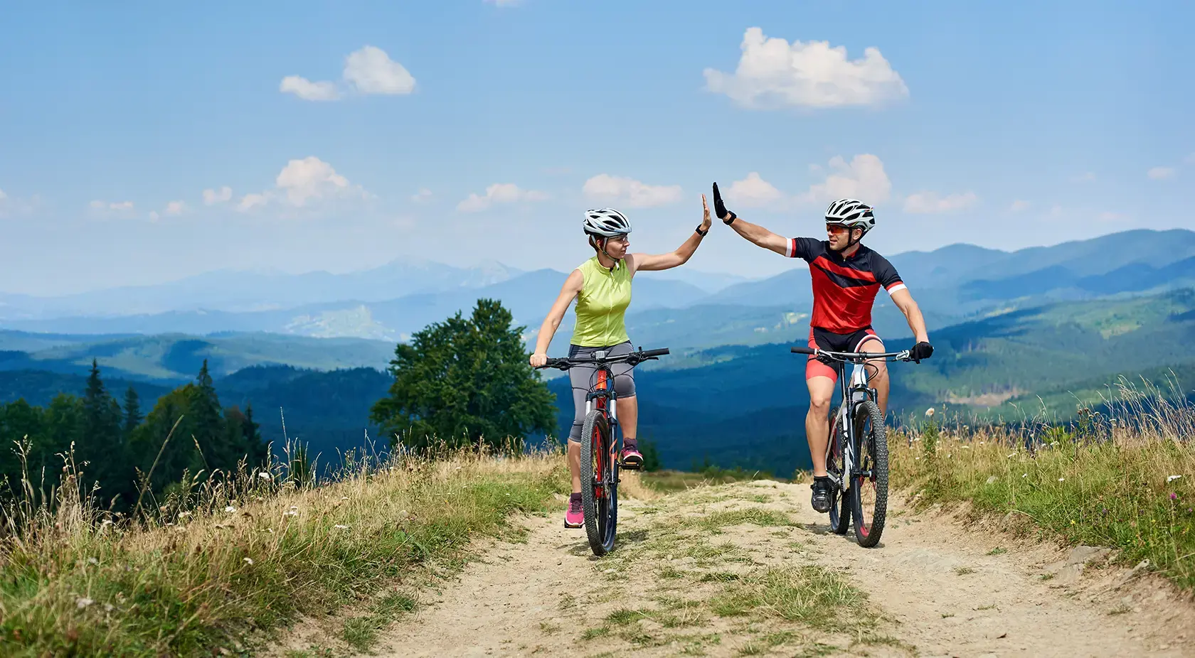 two people riding mountain bikes through the hills giving a high five