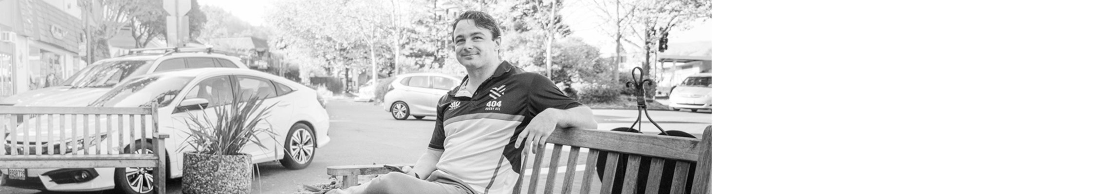 Man reclines on outdoor bench in front of a parking lot.
