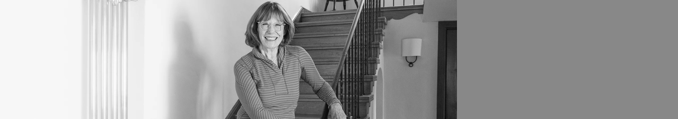 Woman smiling, stands on staircase in her home.