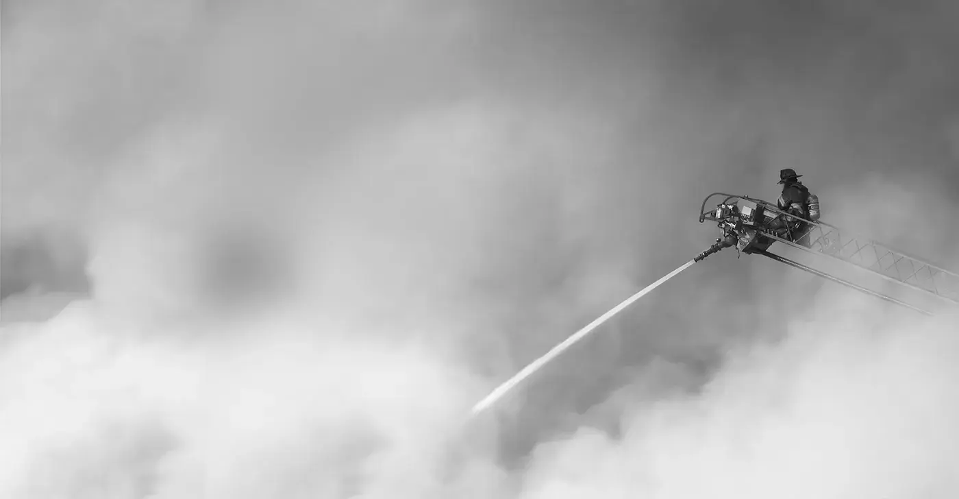 Keeping credit unions safer than banks. Shows a firefighter extinguishing a fire just like SF Fire CU extinguishes fees.